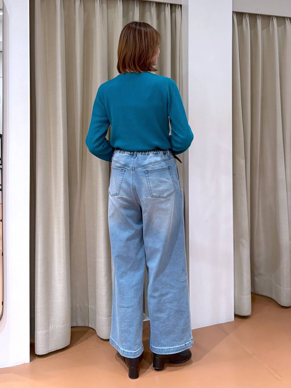 ホワイト系のハンドバッグ、ブラック系のブーツ、ブルー系のデニムパンツを着用したレディースの冬コーディネートの4枚目の写真