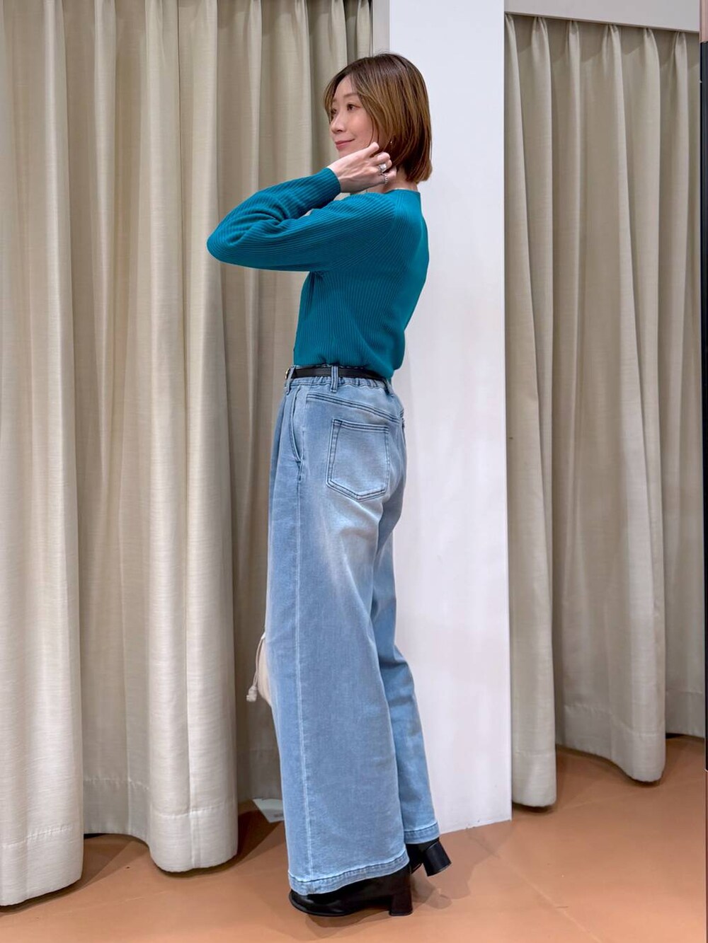 ホワイト系のハンドバッグ、ブラック系のブーツ、ブルー系のデニムパンツを着用したレディースの冬コーディネートの5枚目の写真