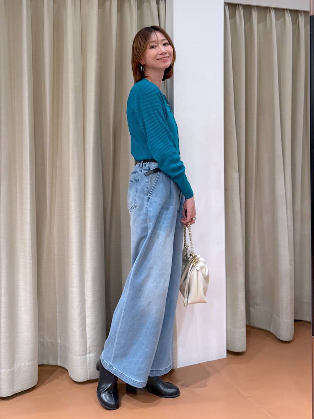 ホワイト系のハンドバッグ、ブラック系のブーツ、ブルー系のデニムパンツを着用したレディースの冬コーディネートの3枚目の写真