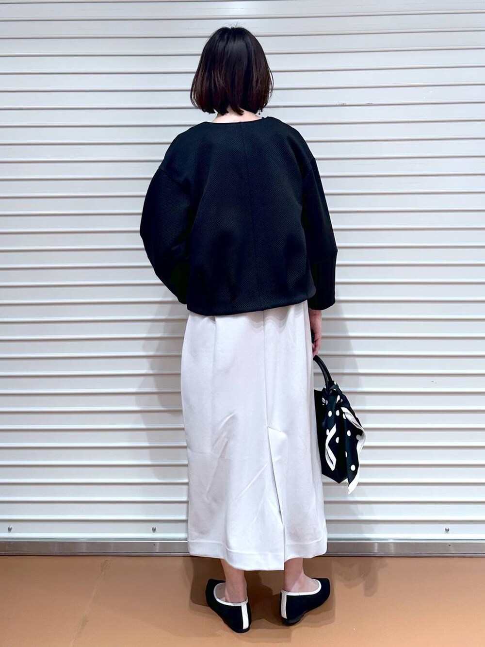 ブラック系のパンプス、ブラック系のショルダーバッグ、ベージュ系のジャンパースカートを着用したレディースの春コーディネートの4枚目の写真