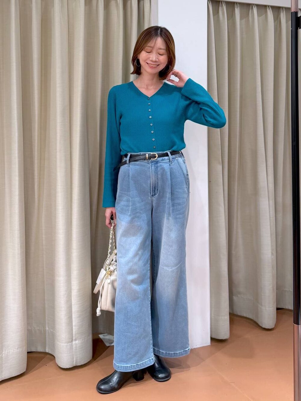 ホワイト系のハンドバッグ、ブラック系のブーツ、ブルー系のデニムパンツを着用したレディースの冬コーディネートの2枚目の写真