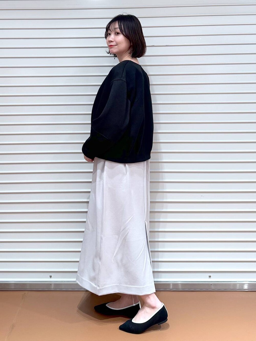ブラック系のパンプス、ブラック系のショルダーバッグ、ベージュ系のジャンパースカートを着用したレディースの春コーディネートの3枚目の写真