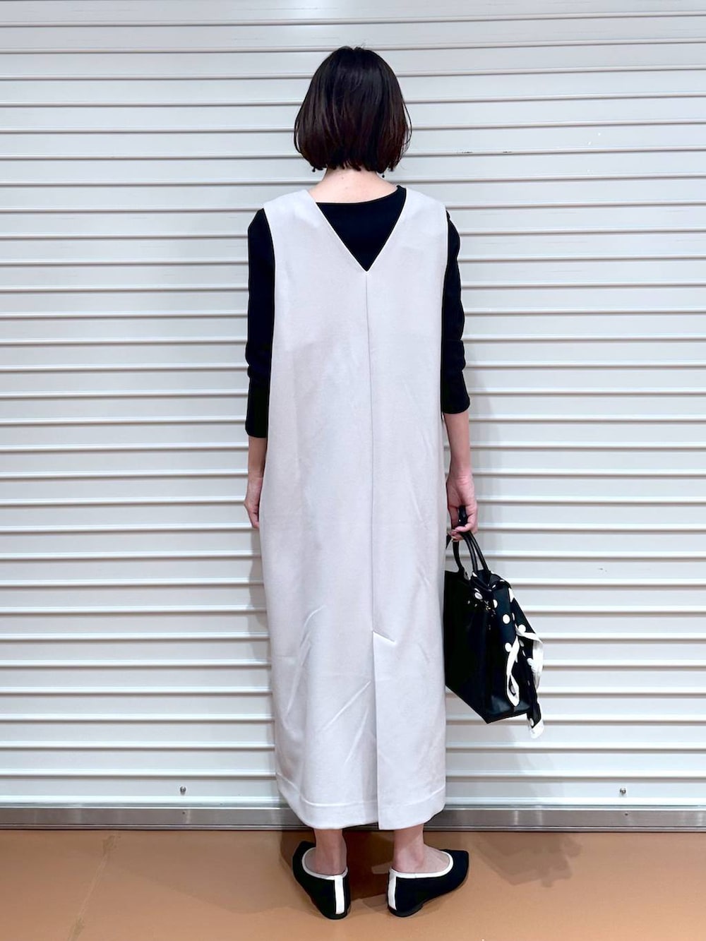 ブラック系のパンプス、ブラック系のショルダーバッグ、ベージュ系のジャンパースカートを着用したレディースの春コーディネートの7枚目の写真