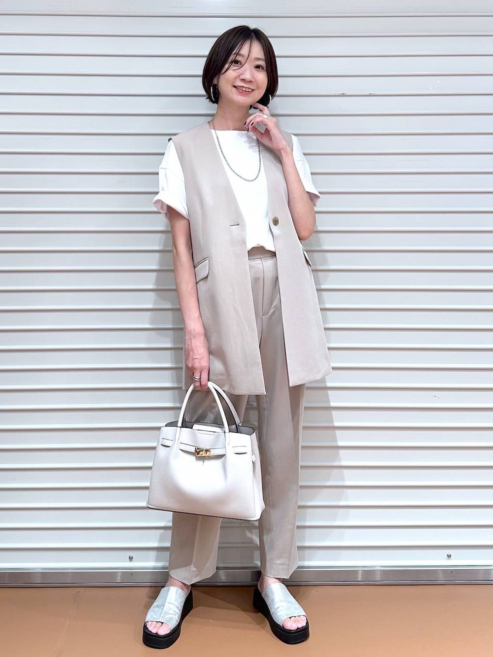 ベージュ系のベスト、シルバー系のサンダル、ホワイト系のTシャツ/カットソーを着用したレディースの夏コーディネートの2枚目の写真