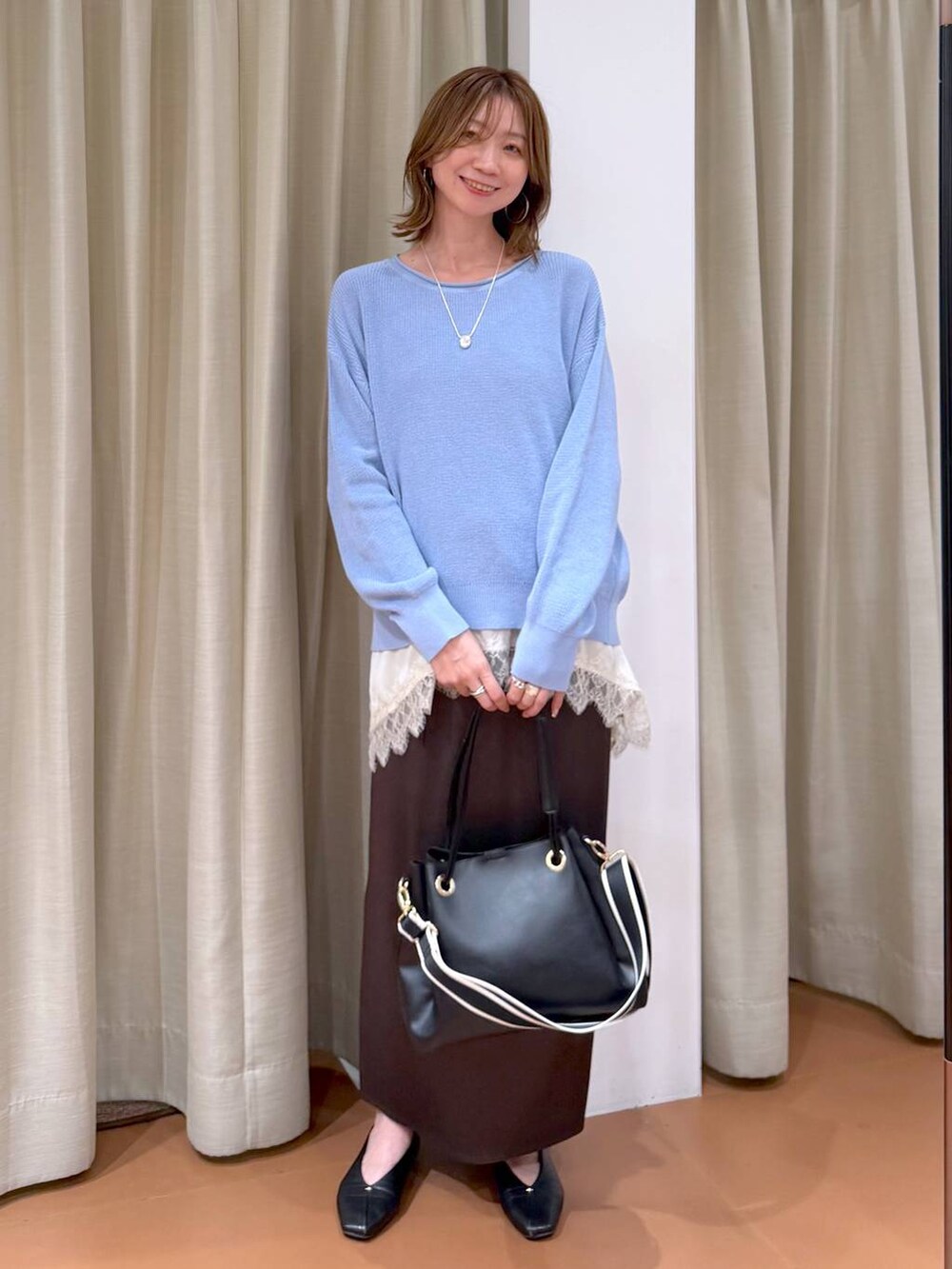 ブルー系のニット/セーター、ブラック系のパンプス、ブラウン系のスカートを着用したレディースの春コーディネートの2枚目の写真