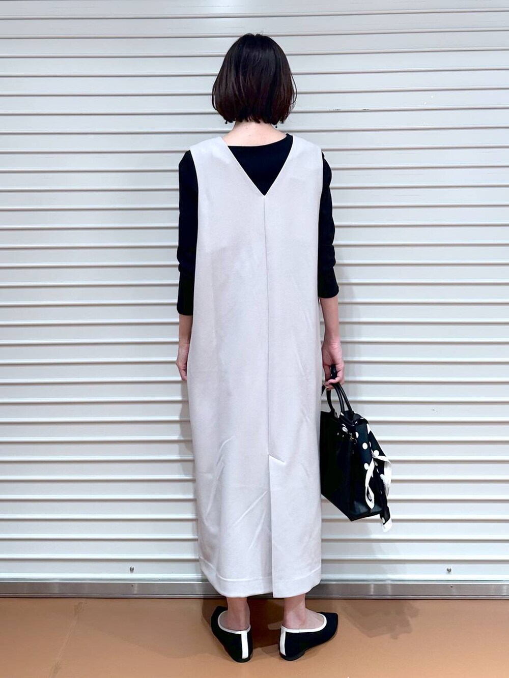 ブラック系のパンプス、ブラック系のショルダーバッグ、ベージュ系のジャンパースカートを着用したレディースの春コーディネートの4枚目の写真
