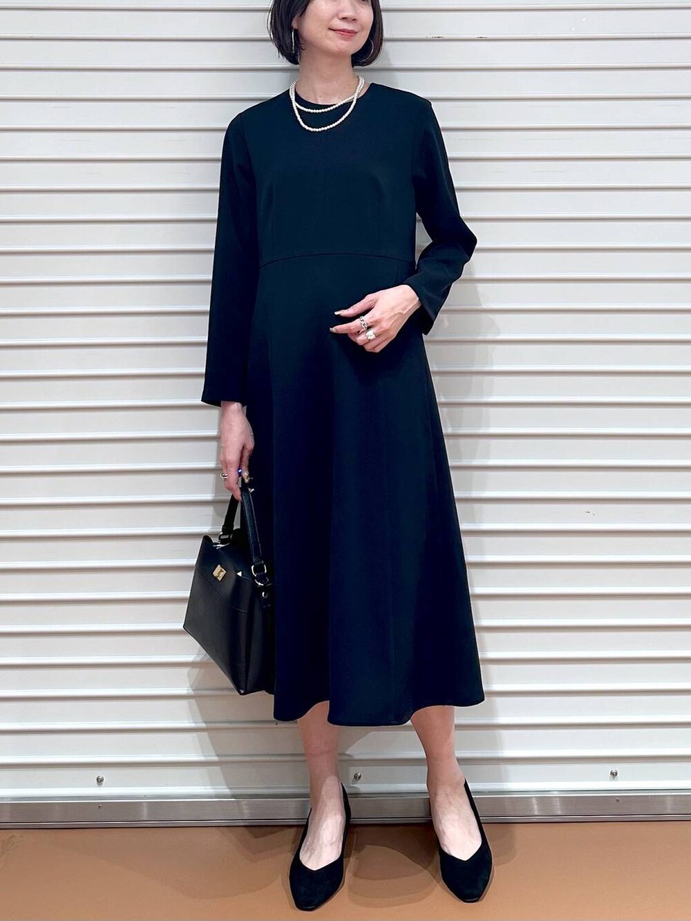 ブルー系のワンピース、ブラック系のハンドバッグ、ブラック系のパンプスを着用したレディースの春コーディネートの3枚目の写真