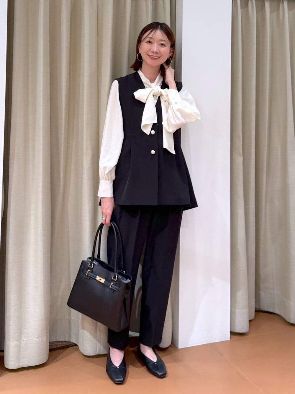 ブラック系のパンプス、ブラック系のスラックス、ブラック系のベストを着用したレディースの冬コーディネートの2枚目の写真