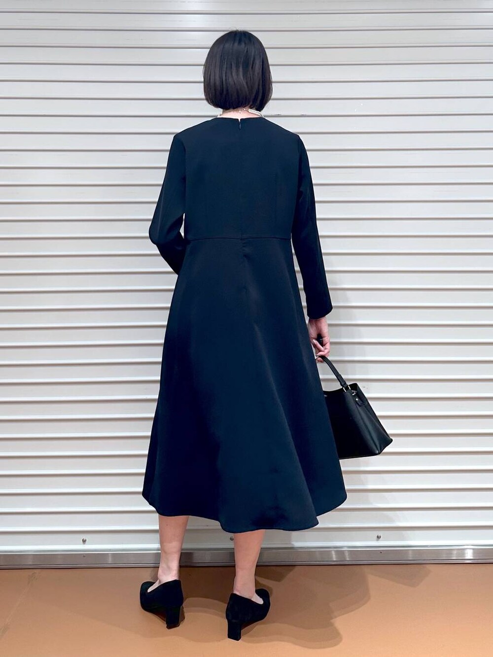 ブルー系のワンピース、ブラック系のハンドバッグ、ブラック系のパンプスを着用したレディースの春コーディネートの2枚目の写真