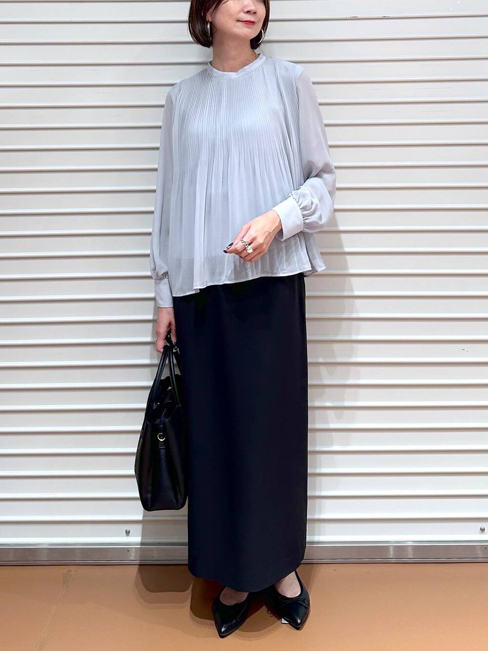 ブラック系のスカート、ブラック系のパンプス、ブラック系のハンドバッグを着用したレディースの秋コーディネートの5枚目の写真