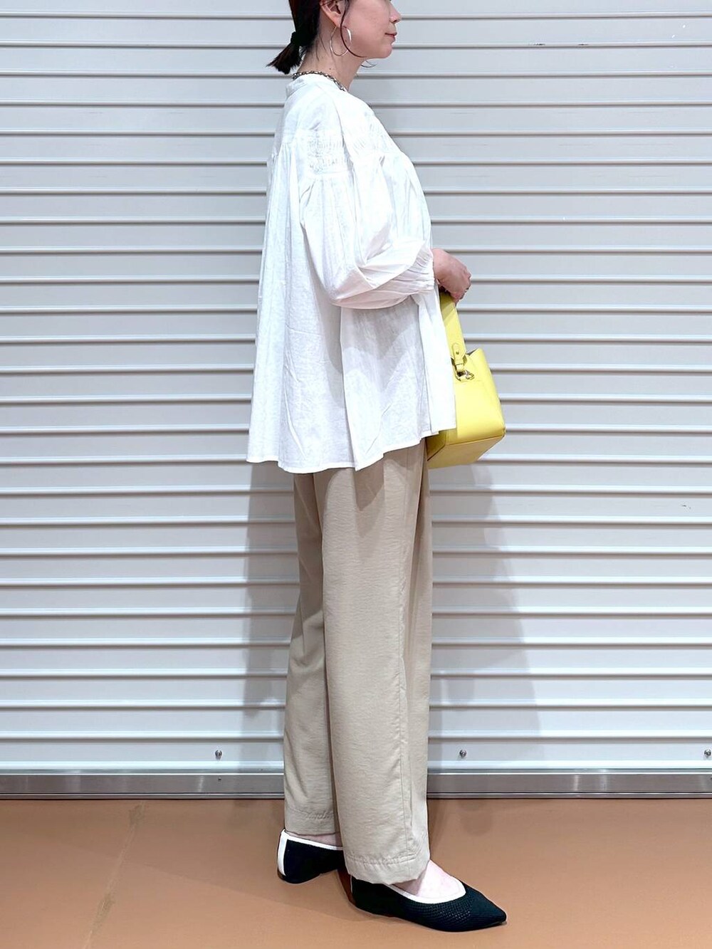 ブラック系のパンプス、ベージュ系のその他パンツ、イエロー系のハンドバッグを着用したレディースの春コーディネートの6枚目の写真