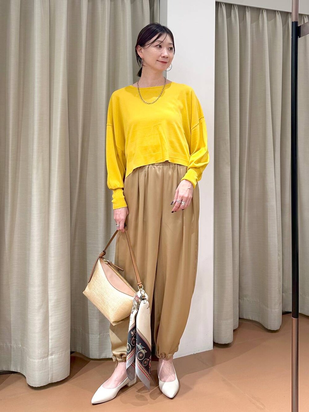 イエロー系のニット/セーター、ブラウン系のその他パンツ、グレー系のネックレスを着用したレディースの春コーディネートの3枚目の写真