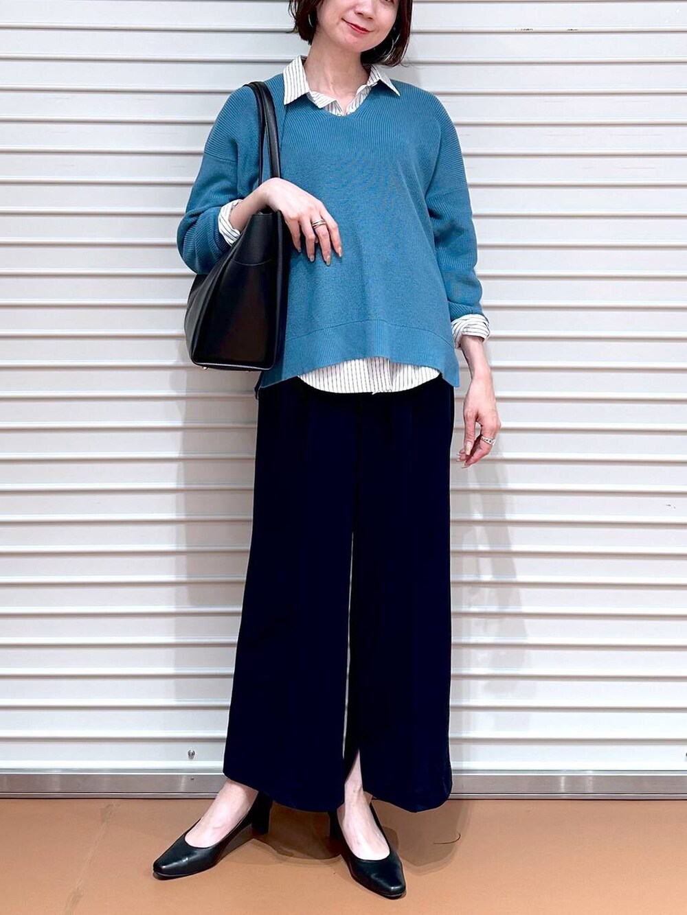 ブラック系のトートバッグ、ブルー系のニット/セーター、ホワイト系のシャツ/ブラウスを着用したレディースの春コーディネートの5枚目の写真