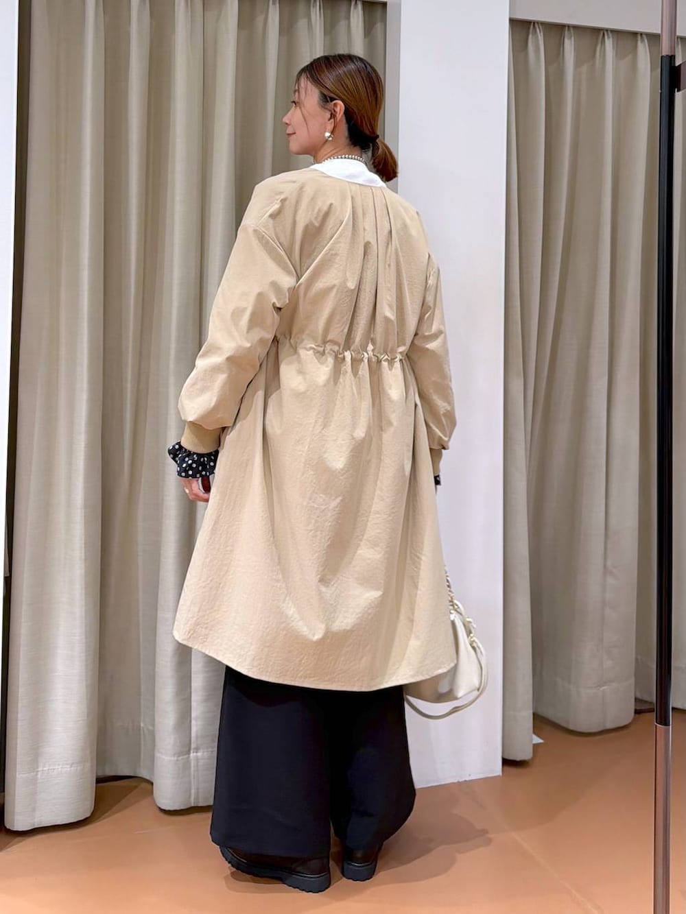 ホワイト系のハンドバッグ、ベージュ系のノーカラーコート、ブラック系のローファーを着用したレディースの冬コーディネートの4枚目の写真