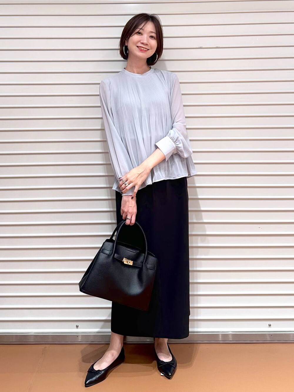 ブラック系のスカート、ブラック系のパンプス、ブラック系のハンドバッグを着用したレディースの秋コーディネートの2枚目の写真