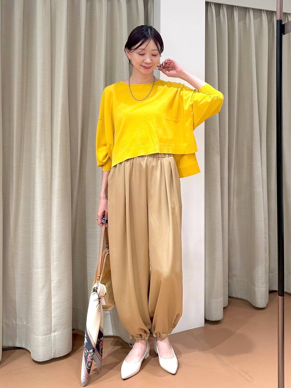 イエロー系のニット/セーター、ブラウン系のその他パンツ、グレー系のネックレスを着用したレディースの春コーディネートの2枚目の写真