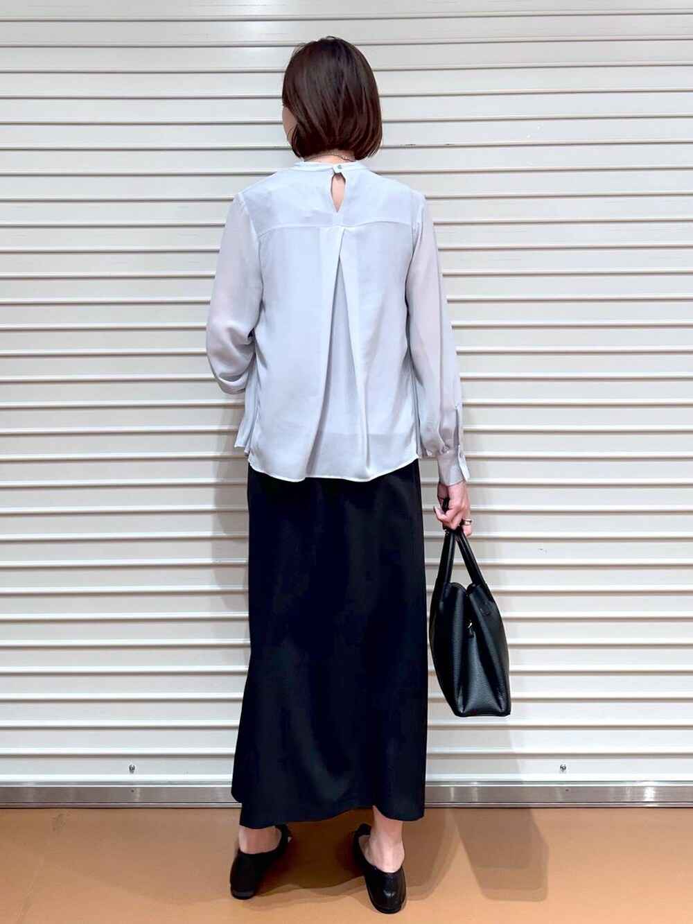 ブラック系のスカート、ブラック系のパンプス、ブラック系のハンドバッグを着用したレディースの秋コーディネートの4枚目の写真