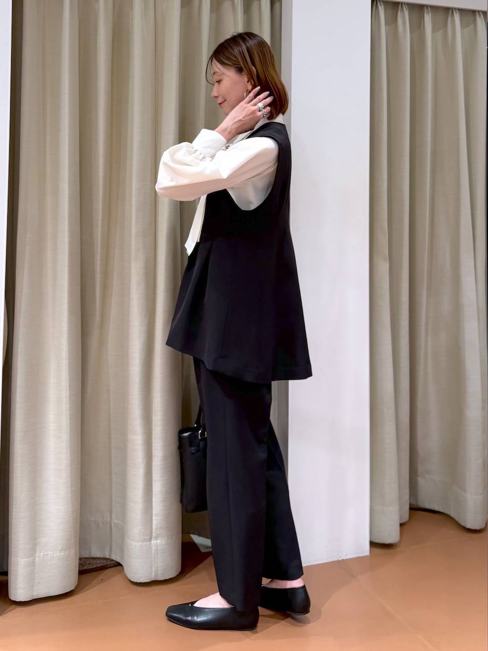 ブラック系のパンプス、ブラック系のスラックス、ブラック系のベストを着用したレディースの冬コーディネートの3枚目の写真