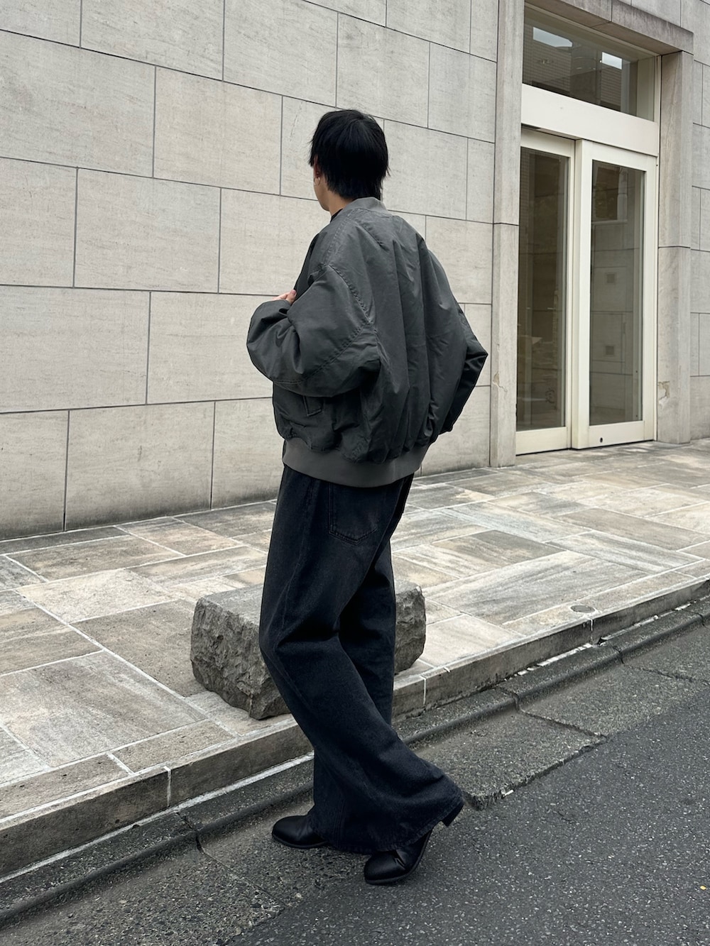 グレー系のブルゾン、ブラック系のTシャツ/カットソー、ブラック系のデニムパンツを着用したメンズの秋コーディネートの2枚目の写真