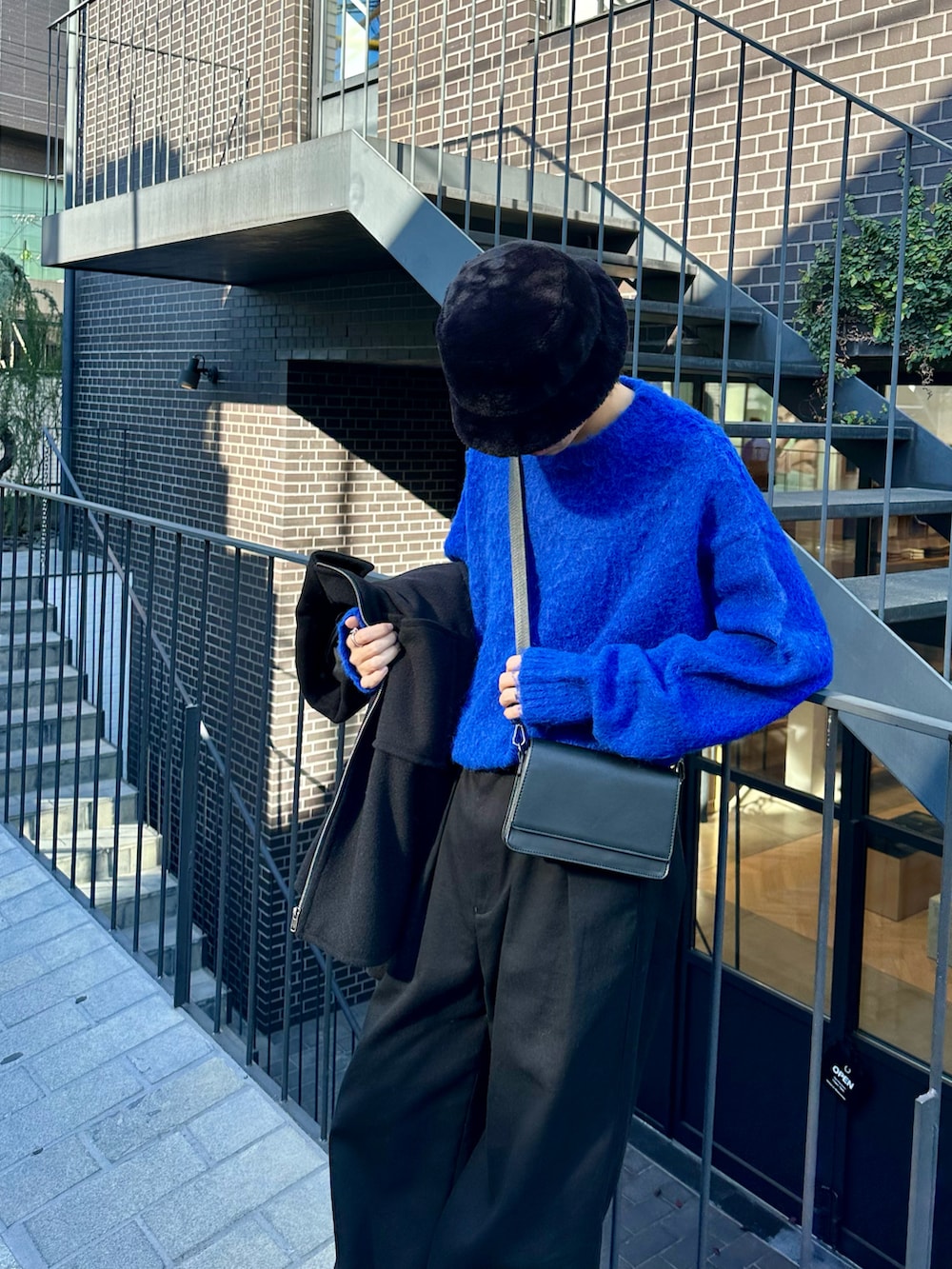 ブラック系のブルゾン、ブルー系のニット/セーター、ブラック系のスラックスを着用したメンズの秋コーディネートの3枚目の写真