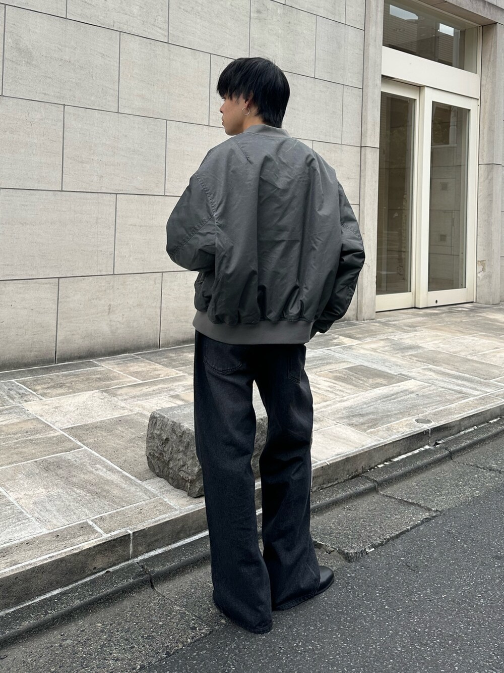 グレー系のブルゾン、ブラック系のTシャツ/カットソー、ブラック系のデニムパンツを着用したメンズの秋コーディネートの3枚目の写真