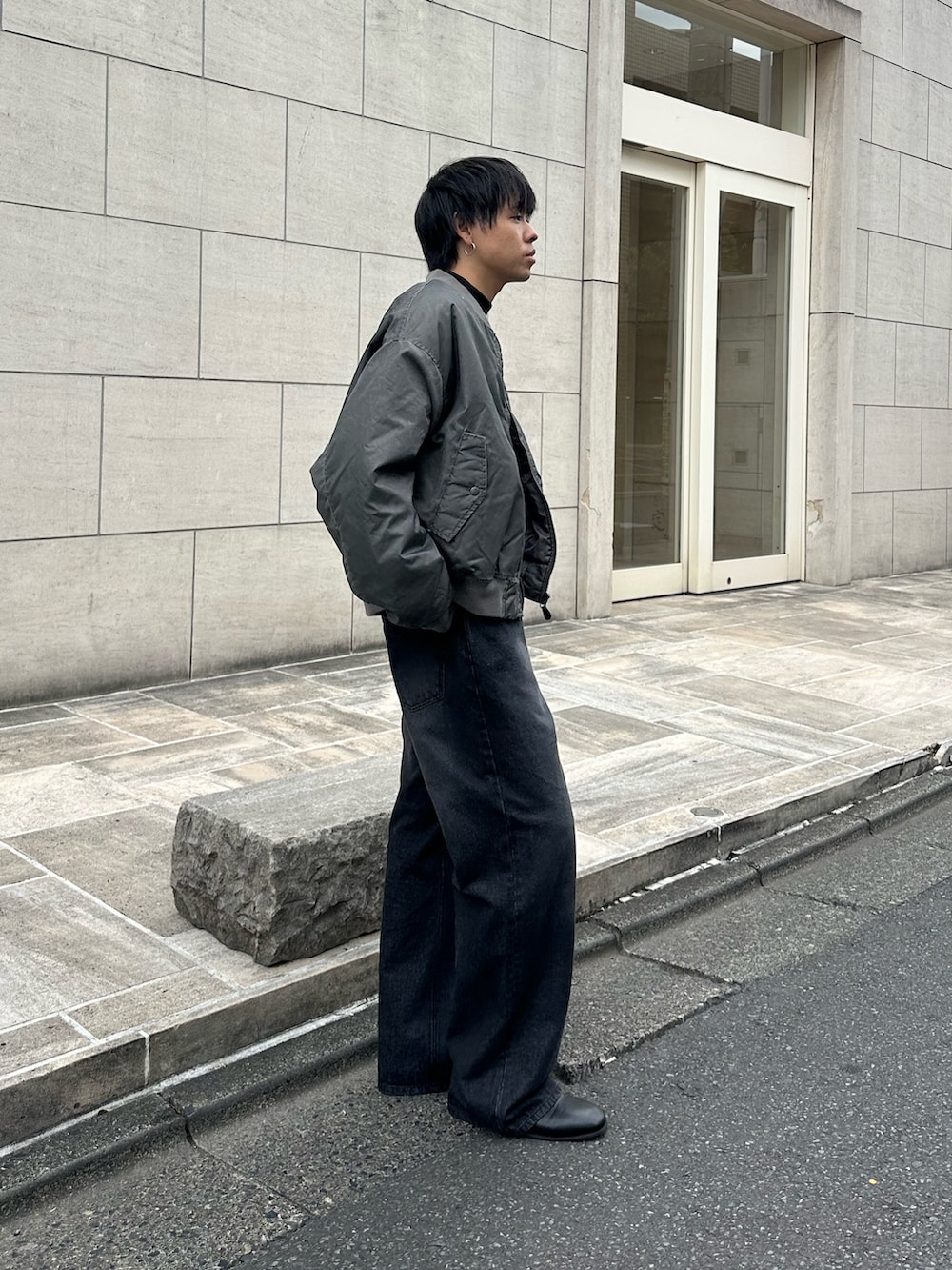 グレー系のブルゾン、ブラック系のTシャツ/カットソー、ブラック系のデニムパンツを着用したメンズの秋コーディネートの4枚目の写真