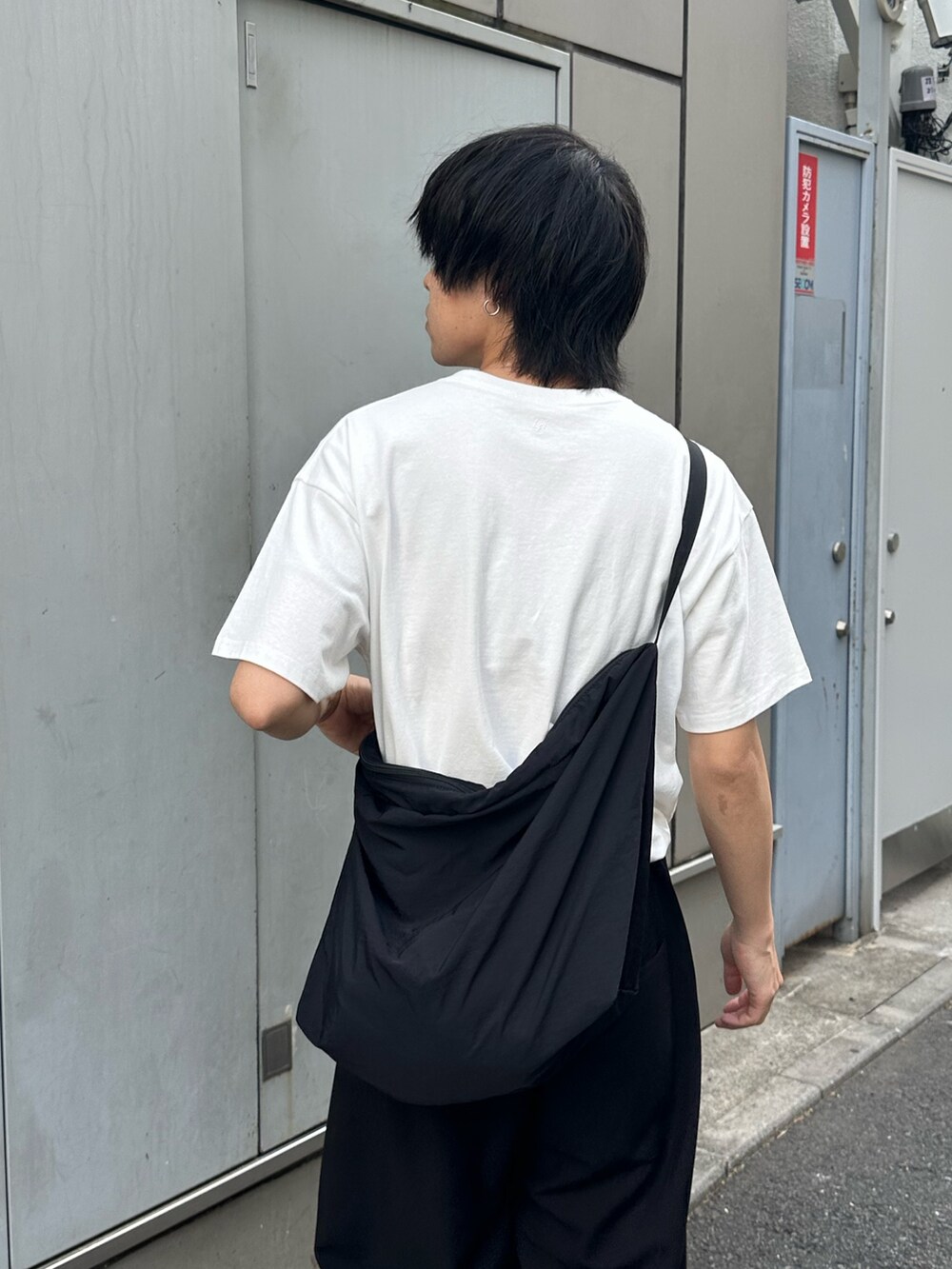 ブラック系のスラックス、ブラック系のショルダーバッグ、ホワイト系のTシャツ/カットソーを着用したメンズの春コーディネートの3枚目の写真