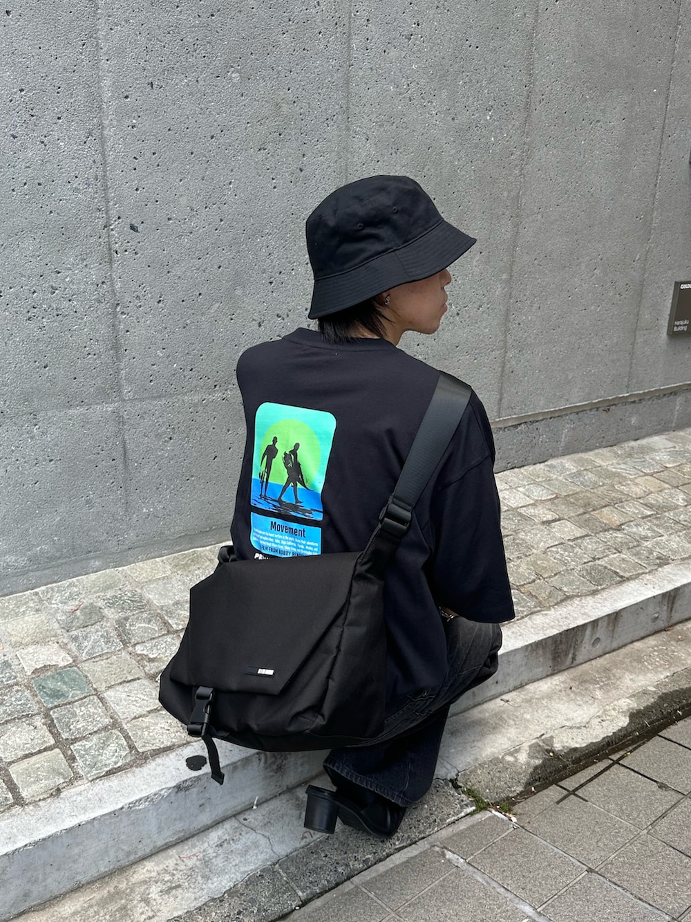 ブラック系のメッセンジャーバッグ、ブラック系のTシャツ/カットソー、ブラック系のデニムパンツを着用したメンズの夏コーディネートの5枚目の写真