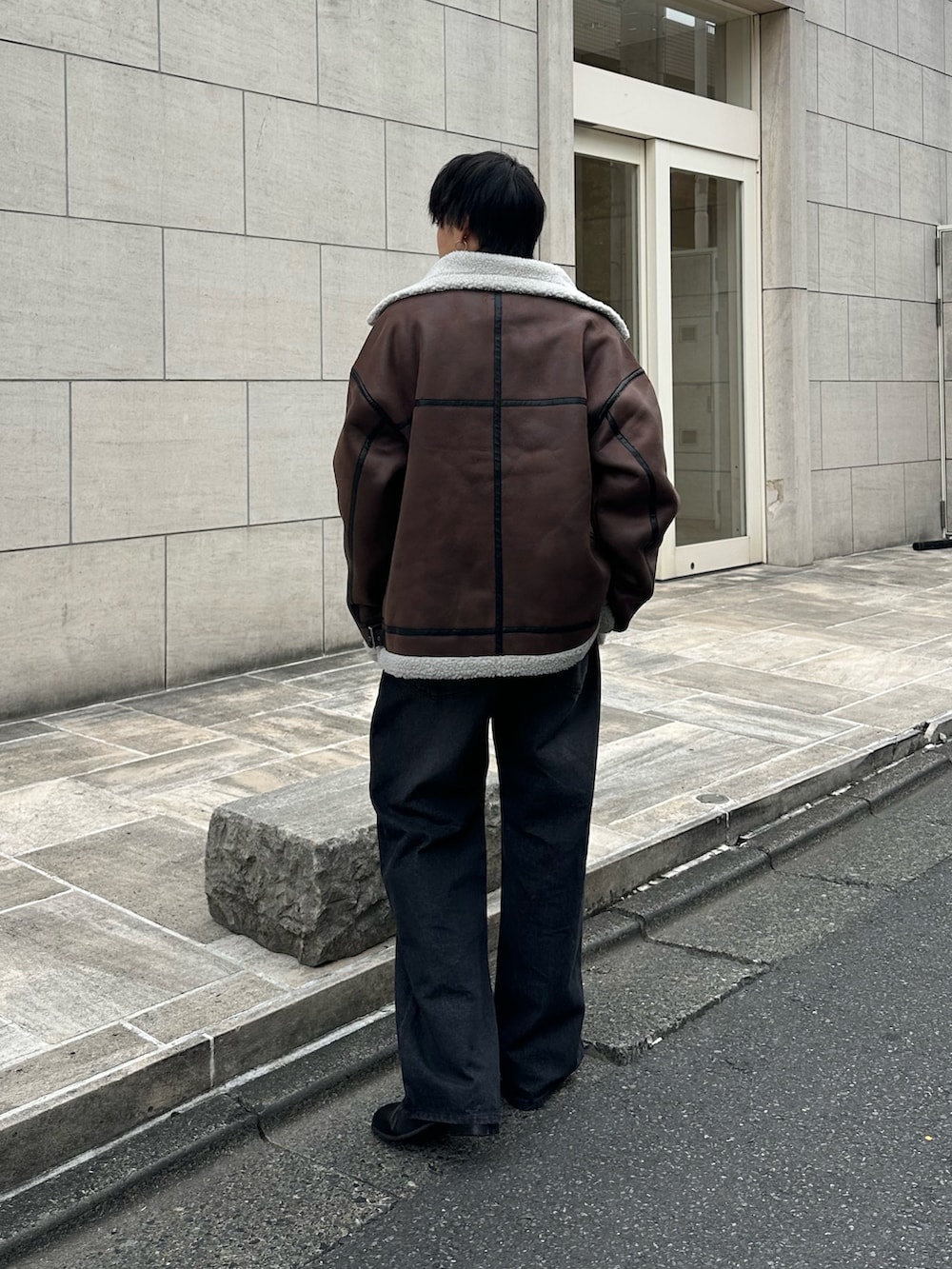 ブラウン系のムートンコート、ブラック系のTシャツ/カットソー、ブラック系のデニムパンツを着用したメンズの秋コーディネートの3枚目の写真