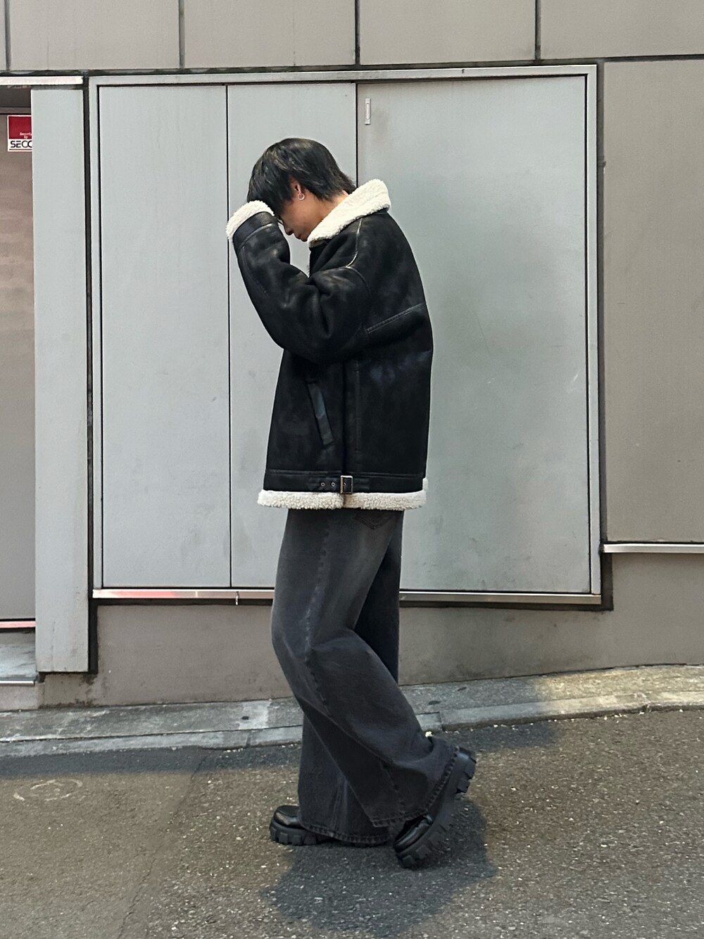 ブラック系のムートンコート、ブラック系のニット/セーター、ブラック系のデニムパンツを着用したメンズの冬コーディネートの4枚目の写真