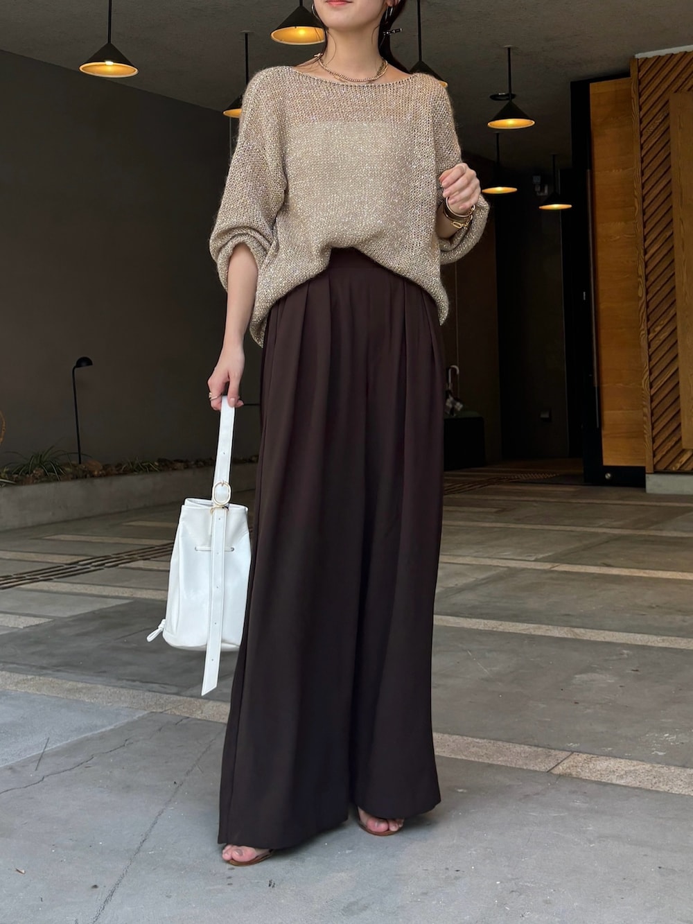 ブラウン系のスラックス、ベージュ系のニット/セーター、ホワイト系のショルダーバッグを着用したレディースの夏コーディネートの2枚目の写真