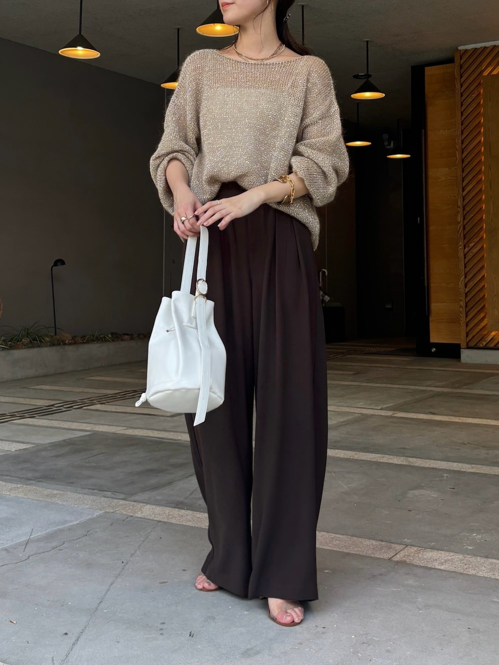 ブラウン系のスラックス、ベージュ系のニット/セーター、ホワイト系のショルダーバッグを着用したレディースの夏コーディネートの3枚目の写真