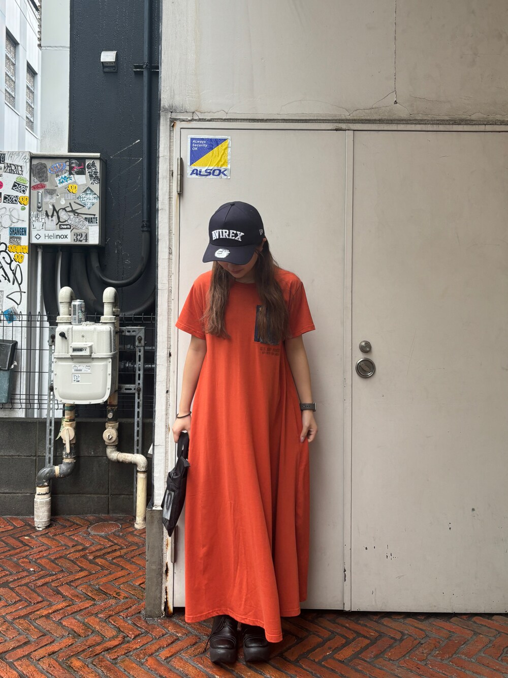 ブラック系のショルダーバッグ、オレンジ系のワンピース/ドレス、ブルー系のキャップを着用したレディースの春コーディネートの2枚目の写真