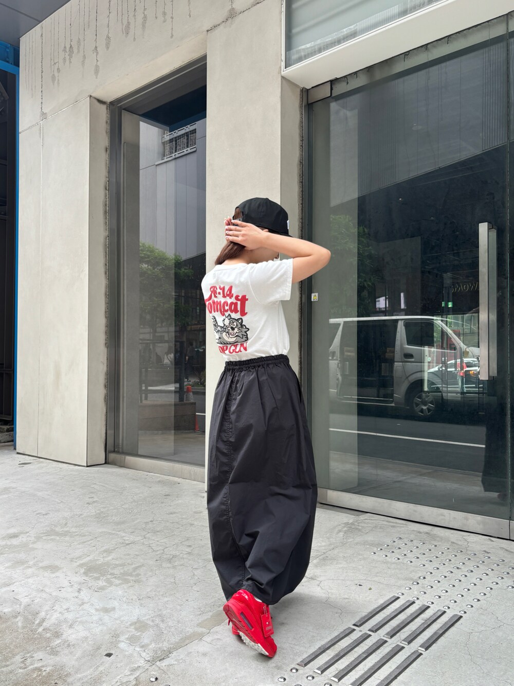 レッド系のTシャツ/カットソー、ブラック系のスカート、ブラック系のキャップを着用したレディースの夏コーディネートの2枚目の写真