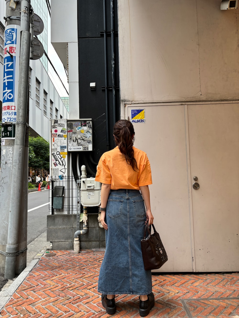 オレンジ系のTシャツ/カットソー、ブラウン系のトートバッグを着用したレディースの夏コーディネートの2枚目の写真