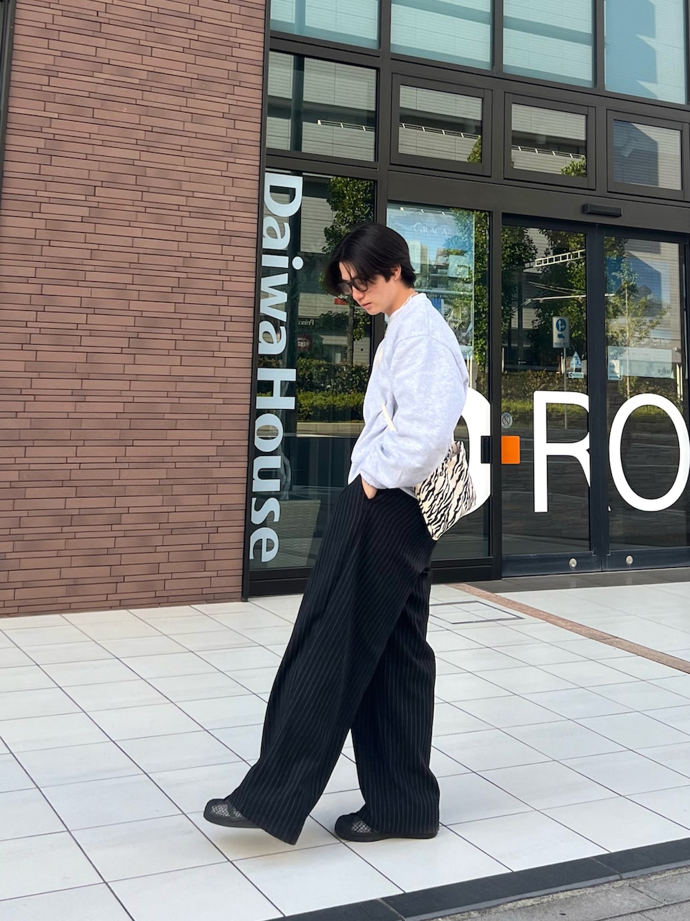 グレー系のスウェット、ブラック系のスラックス、ブラック系のスニーカーを着用したメンズの春コーディネートの2枚目の写真