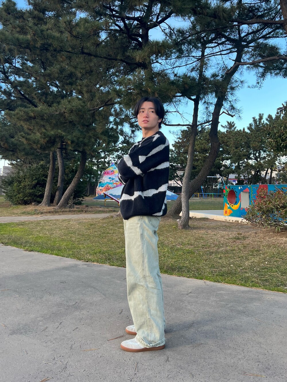 ブラック系のニット/セーター、グリーン系のチノパンツ、ホワイト系のスニーカーを着用したメンズの春コーディネートの3枚目の写真