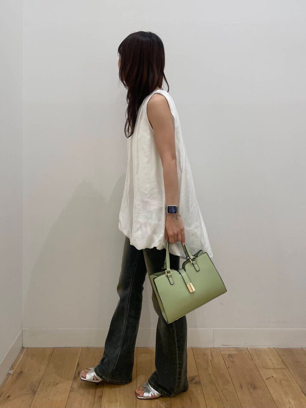グリーン系のハンドバッグ、シルバー系のサンダル、ブルー系のデニムパンツを着用したレディースの春コーディネートの2枚目の写真