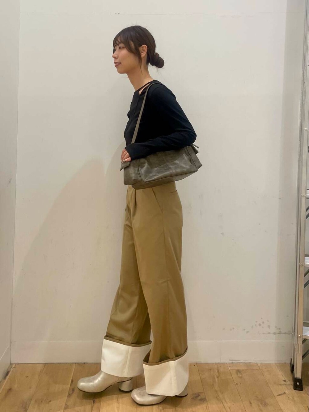 グレー系のハンドバッグ、ゴールド系のブーツ、ブラック系のTシャツ/カットソーを着用したレディースの秋コーディネートの2枚目の写真