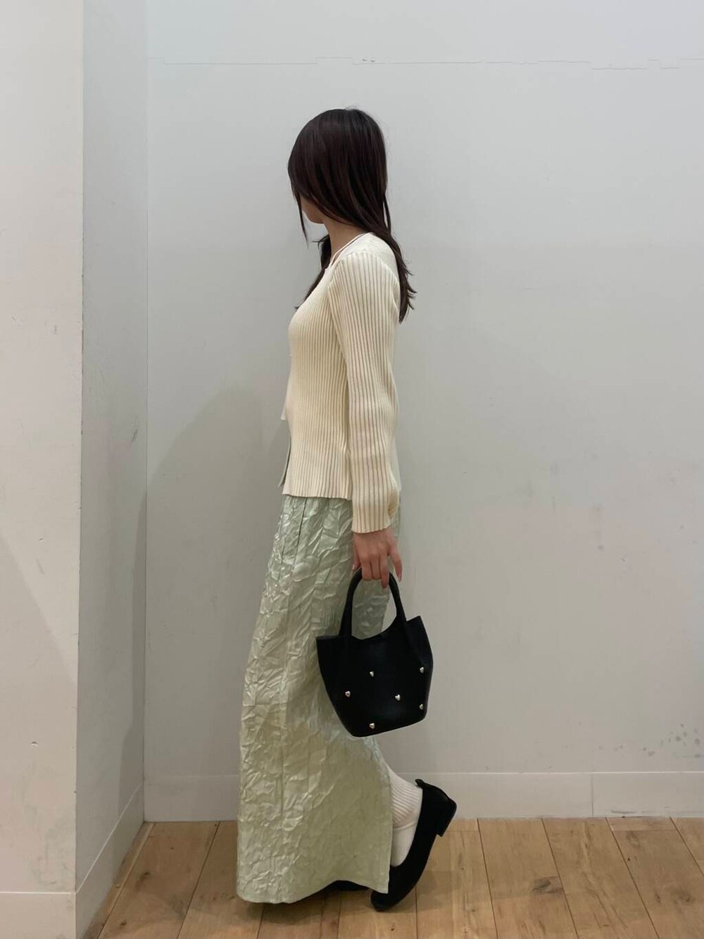 ブラック系のショルダーバッグ、ホワイト系のニット/セーター、グリーン系のスカートを着用したレディースの春コーディネートの2枚目の写真