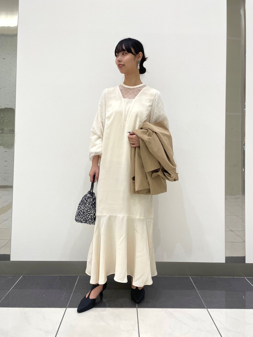 ベージュ系のトレンチコート、ホワイト系のワンピース、ブラック系のパンプスを着用したレディースの春コーディネートの2枚目の写真