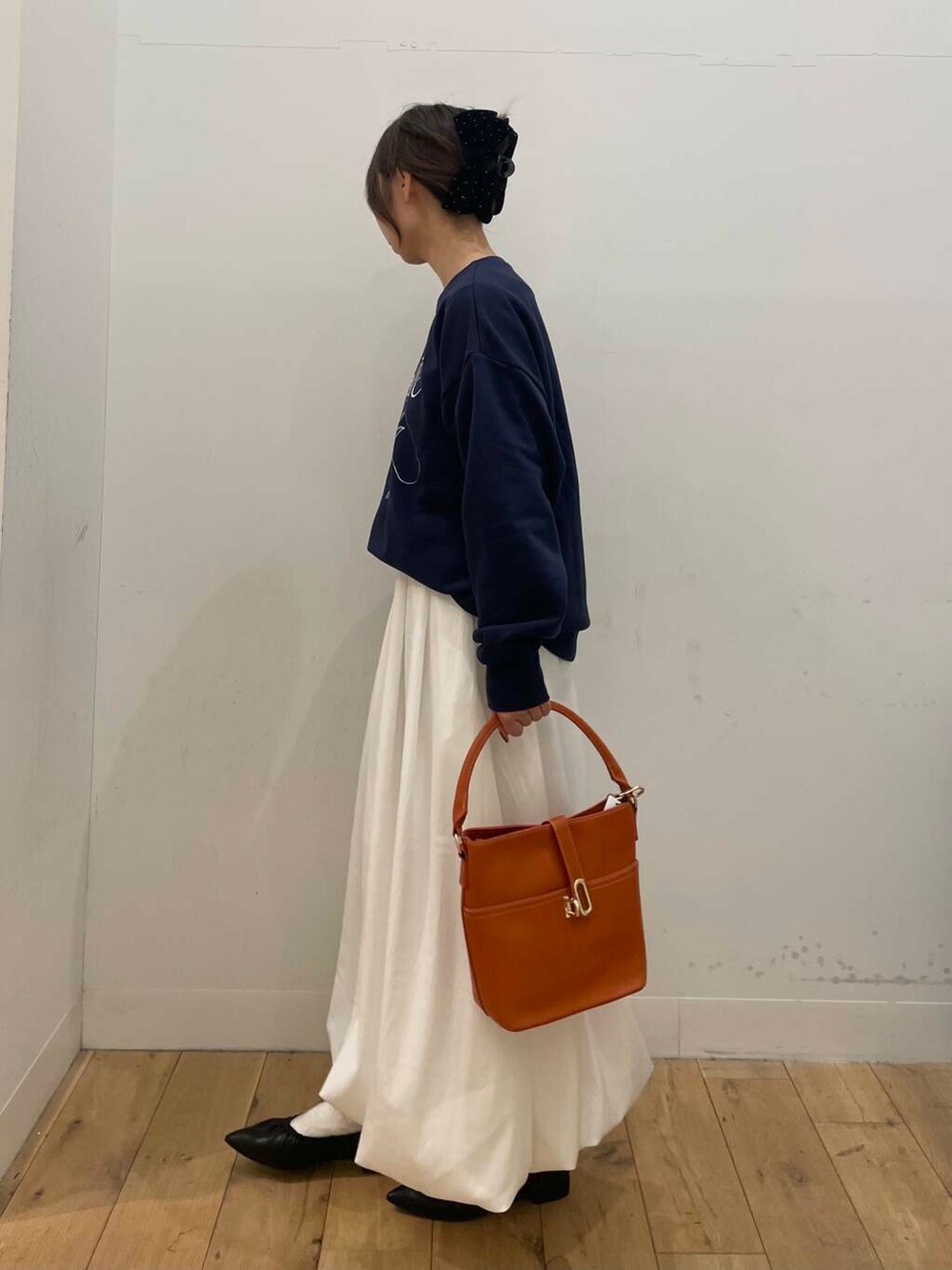 オレンジ系のハンドバッグ、ホワイト系のスカート、ブラック系のパンプスを着用したレディースの冬コーディネートの2枚目の写真