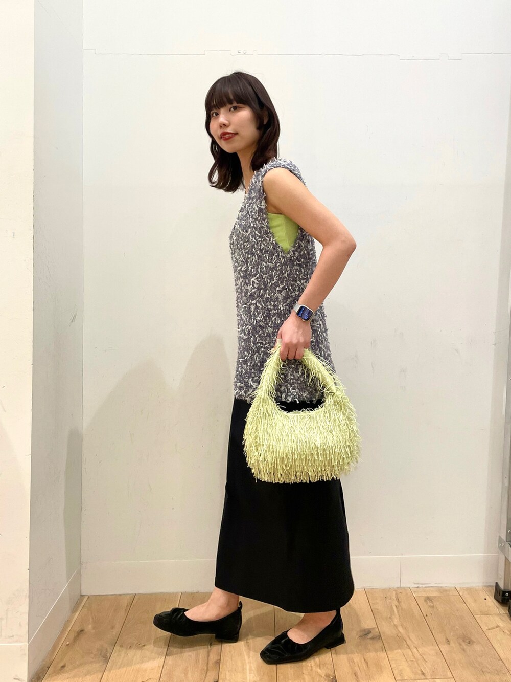 ブラック系のパンプス、ブラック系のスカート、グリーン系のハンドバッグを着用したレディースの春コーディネートの2枚目の写真