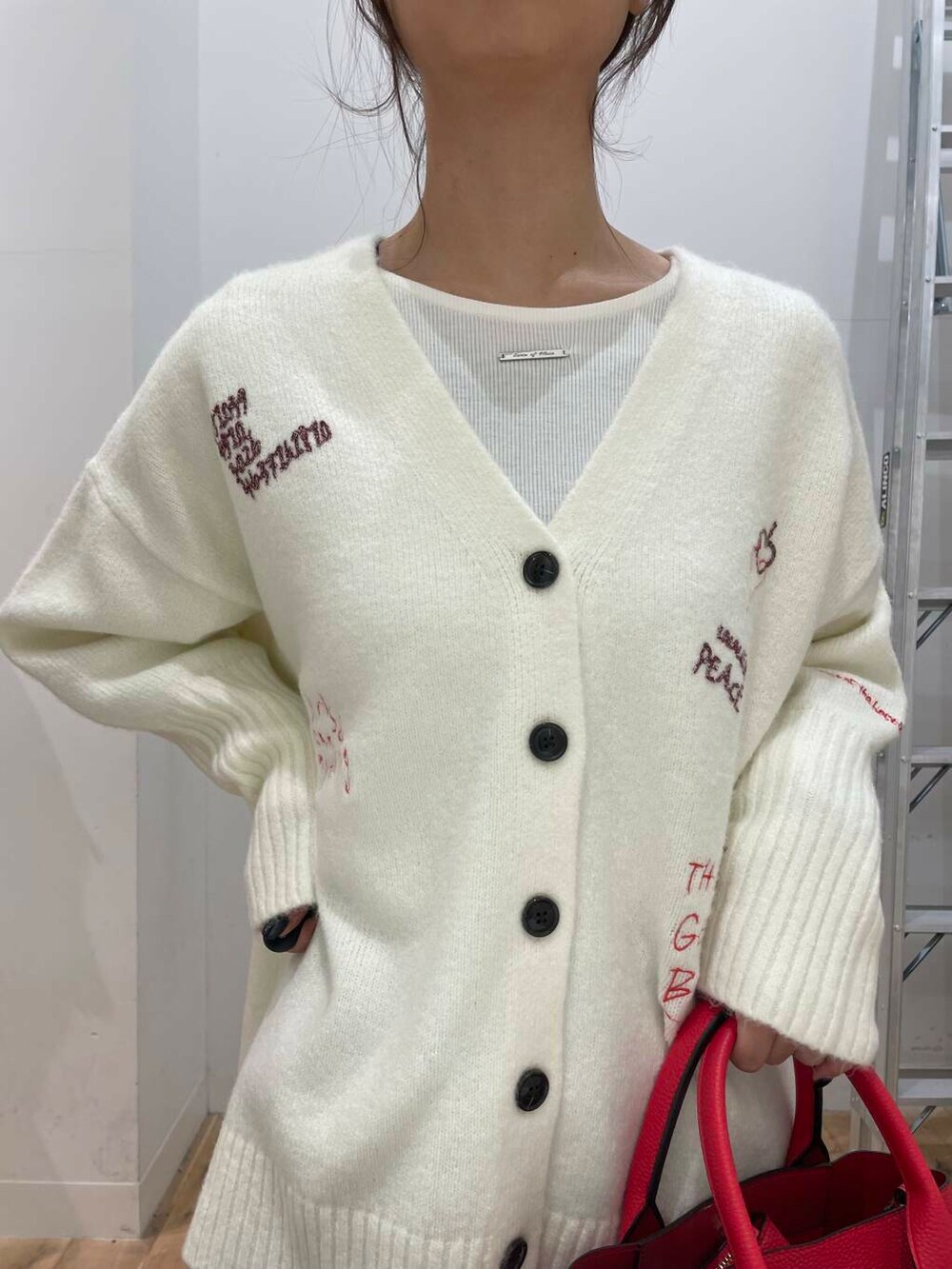 レッド系のトートバッグ、ホワイト系のTシャツ/カットソー、ホワイト系のカーディガン/ボレロを着用したレディースの冬コーディネートの4枚目の写真