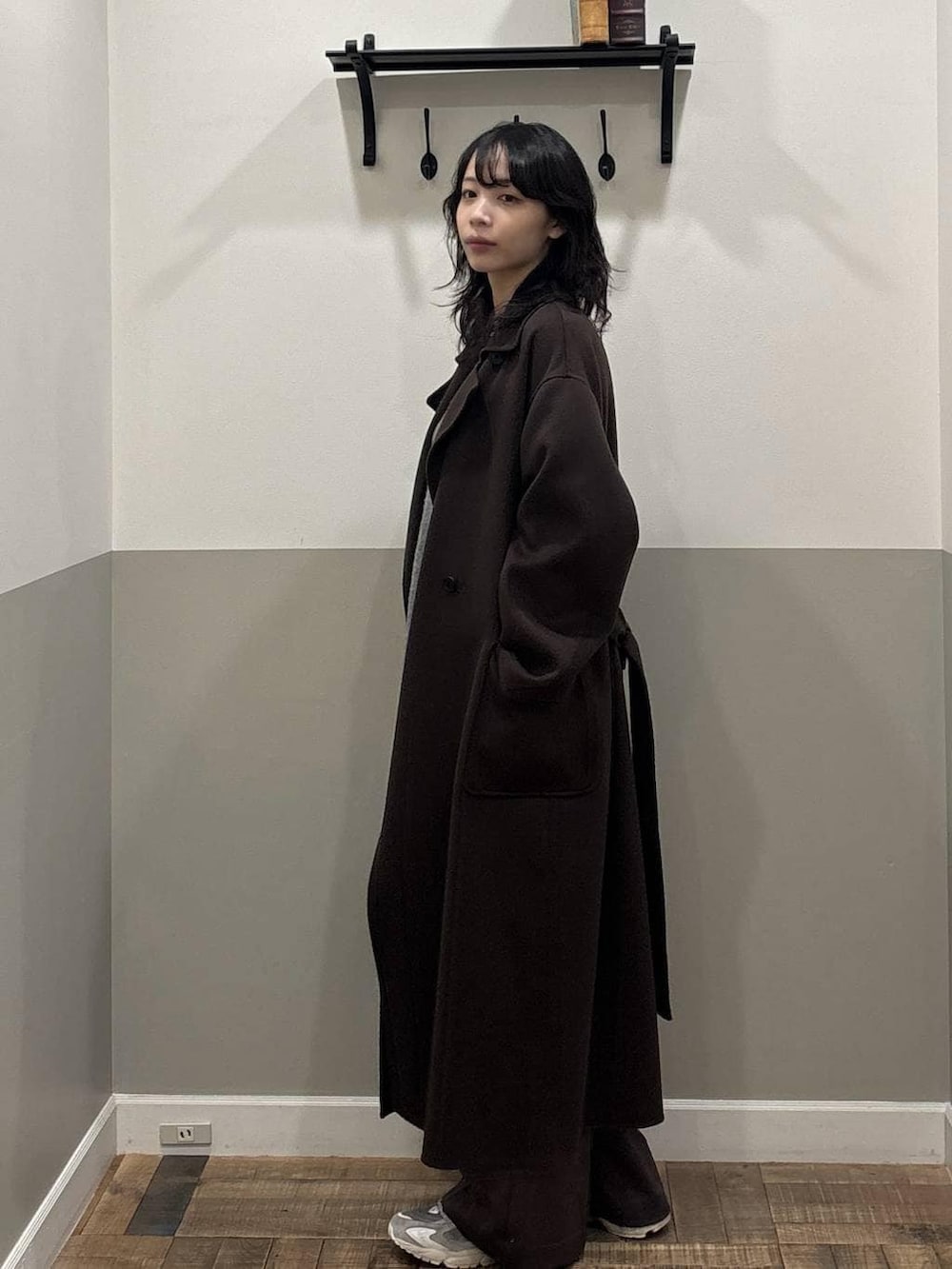 ブラウン系のステンカラーコート、グレー系のカーディガン/ボレロ、グリーン系のショルダーバッグを着用したレディースの秋コーディネートの2枚目の写真