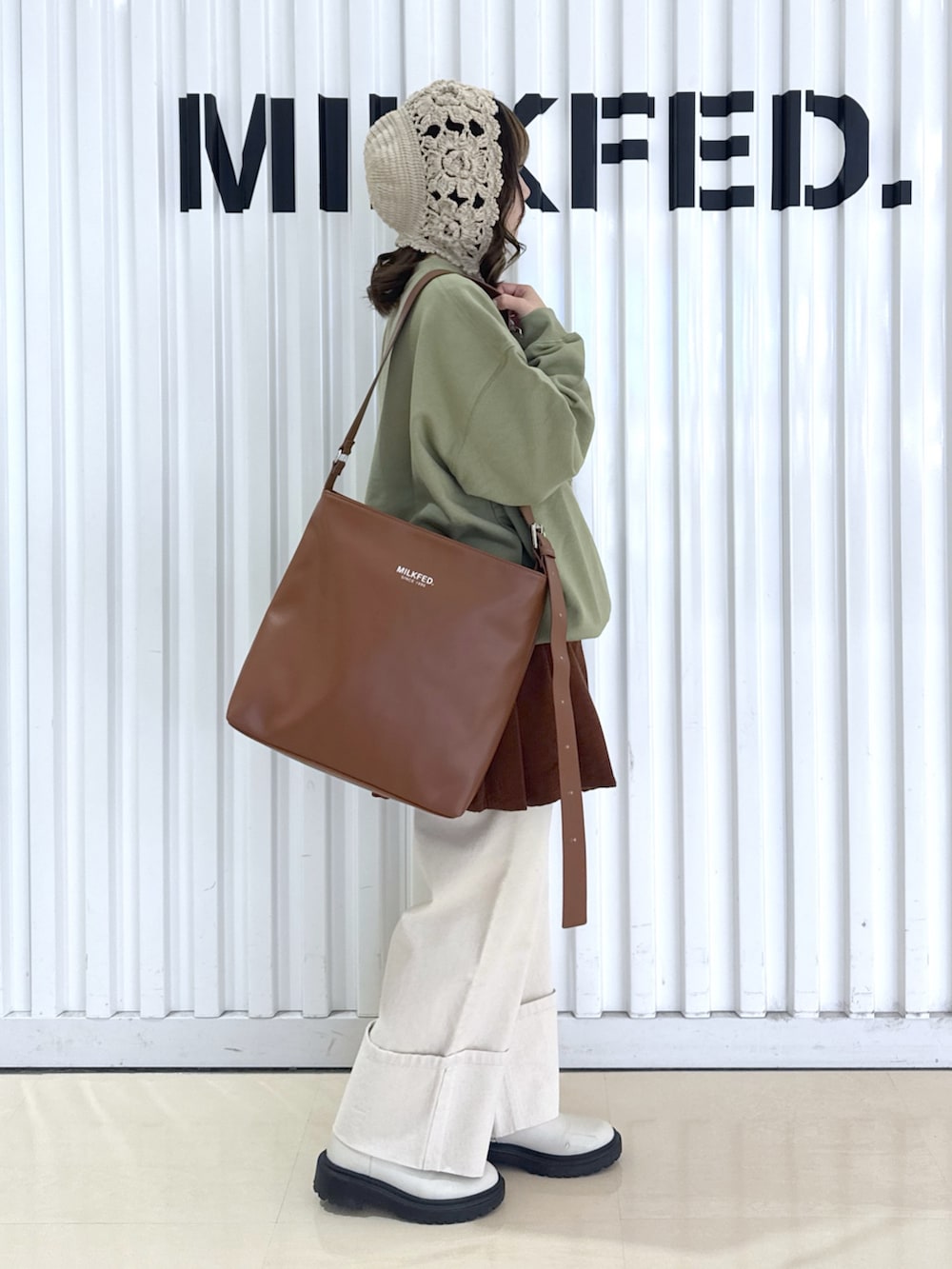 ホワイト系のデニムパンツ、グリーン系のスウェット、ブラウン系のショルダーバッグを着用したレディースの冬コーディネートの3枚目の写真