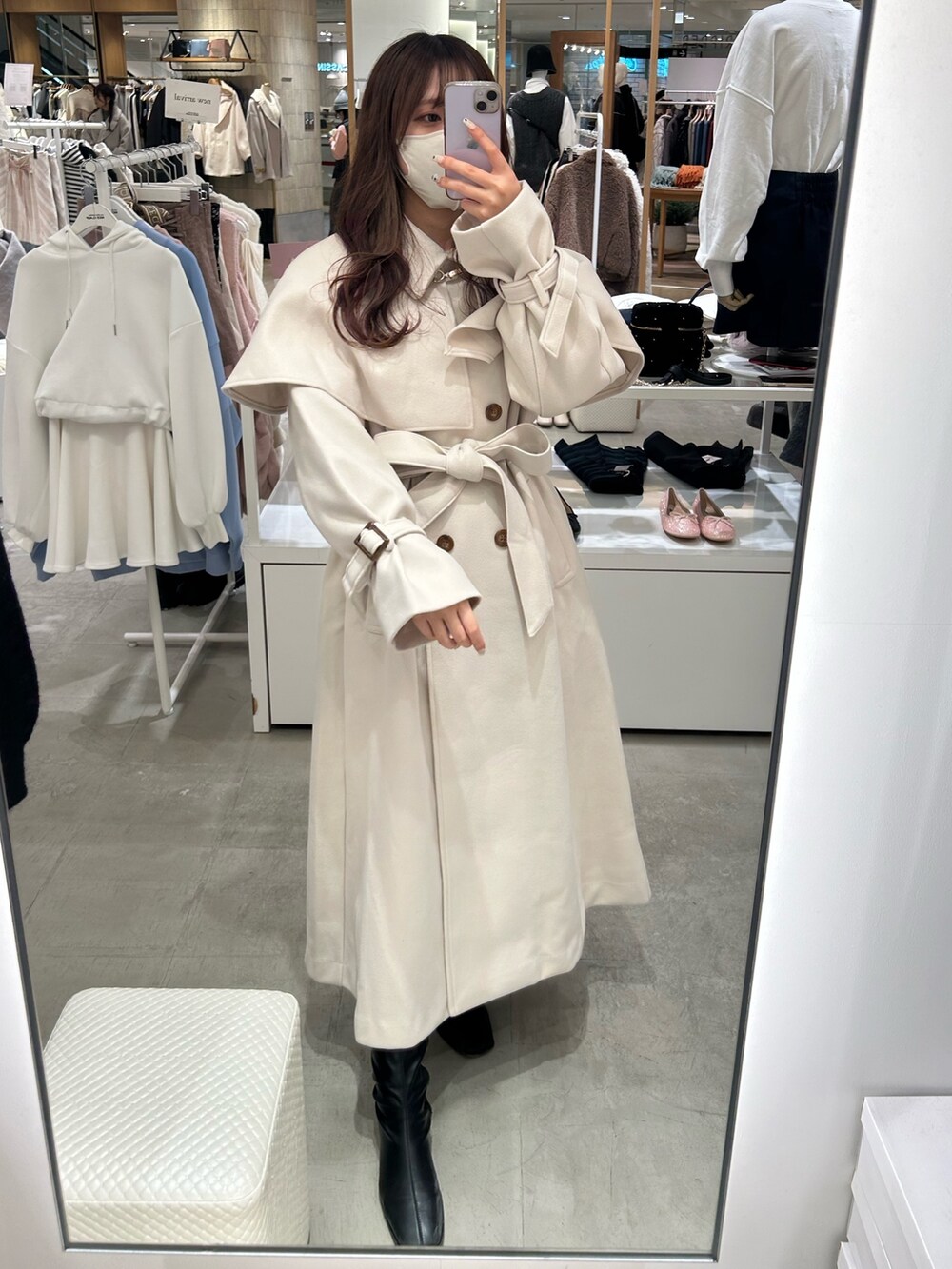 ホワイト系のステンカラーコート、ホワイト系のハンドバッグ、ブラック系のブーツを着用したレディースの秋コーディネートの3枚目の写真