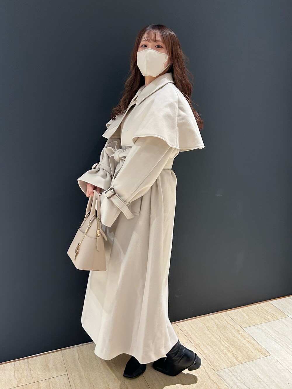 ホワイト系のステンカラーコート、ホワイト系のハンドバッグ、ブラック系のブーツを着用したレディースの秋コーディネートの2枚目の写真