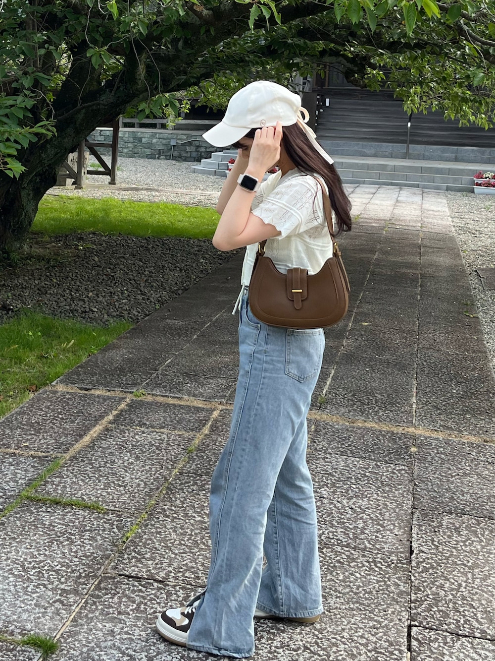 ホワイト系のカーディガン/ボレロ、ブラウン系のショルダーバッグ、ブルー系のデニムパンツを着用したレディースの夏コーディネートの2枚目の写真