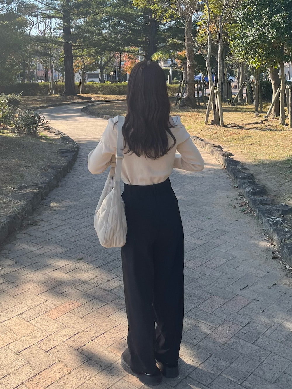 ホワイト系のニット/セーター、ホワイト系のショルダーバッグ、ブラック系のスラックスを着用したレディースの冬コーディネートの2枚目の写真